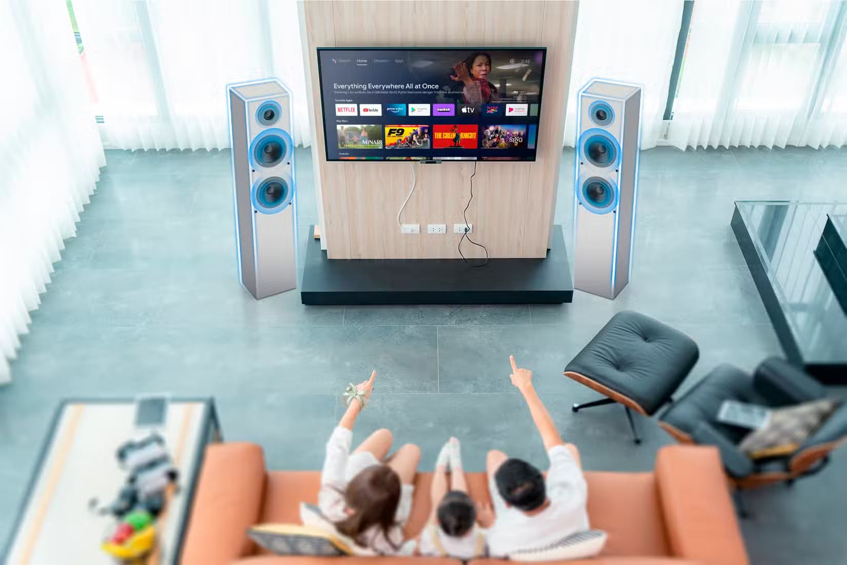 a-family-sitting-on-the-couch-watching-tv-with-the-speakers-highlighted 10 مصطلحات أساسية في الصوت يجب على كل مبتدئ معرفتها