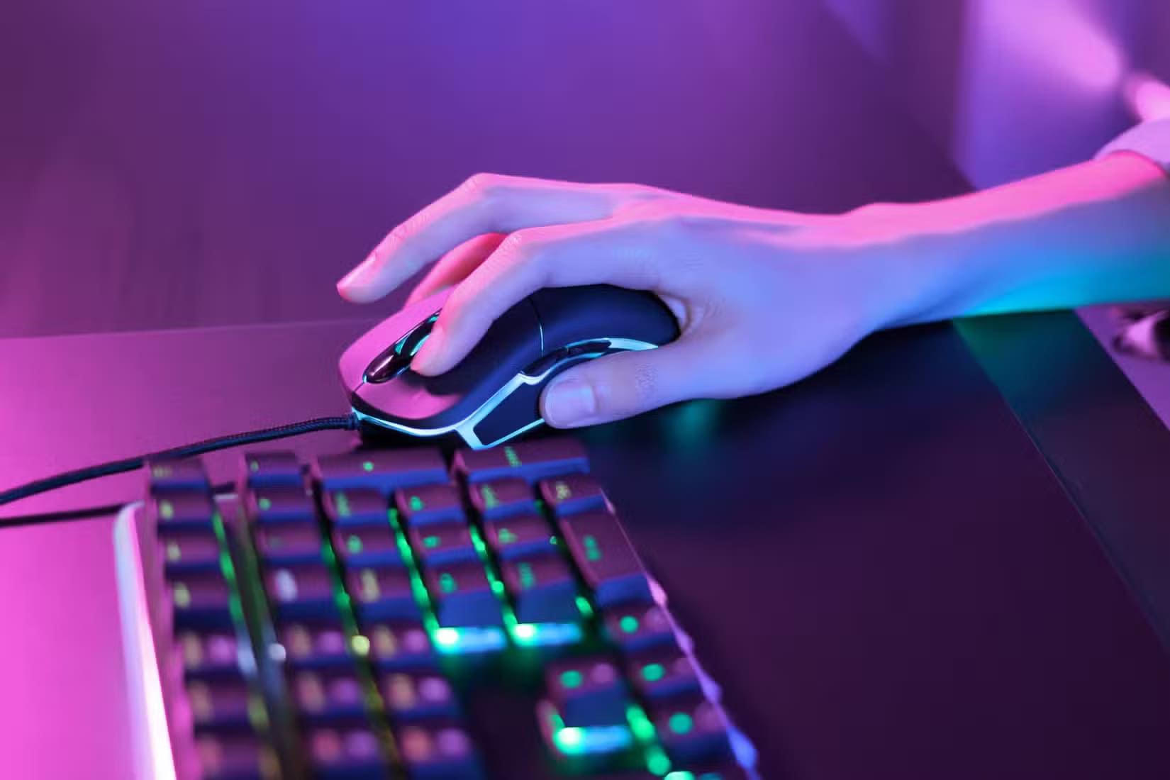 person-using-a-gaming-mouse-under-pink-neon-lights-next-to-an-rgb-keyboard أسباب تفضيل الألعاب التعاونية على التنافسية وكيفية الاستمتاع بها