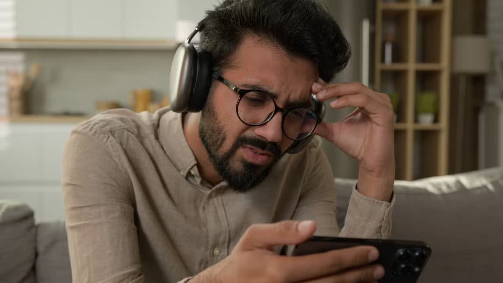 a-frustrated-man-looking-at-an-iphone-with-airpods-max-headphones-on كل ما تحتاج معرفته عن منحنى هارمان وتأثيره على جودة الصوت