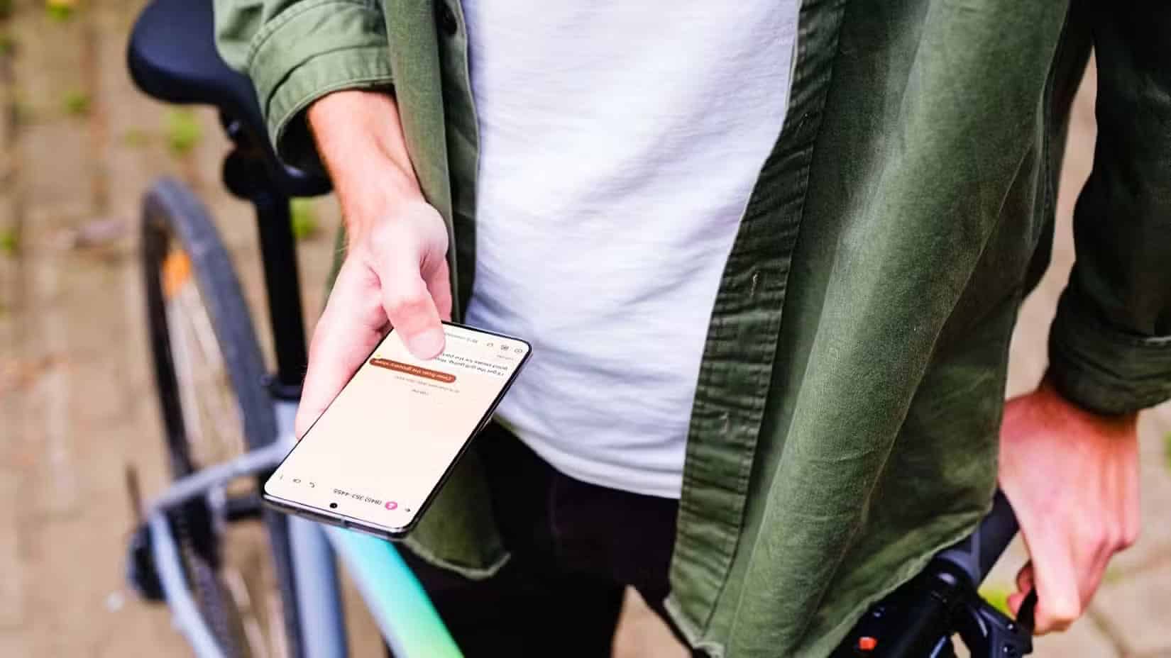 a-person-standing-next-to-a-bike-holding-their-android-device-there-is-a-text-conversation-on-the-phone أهم ميزات Android المخفية التي يجب تجربتها