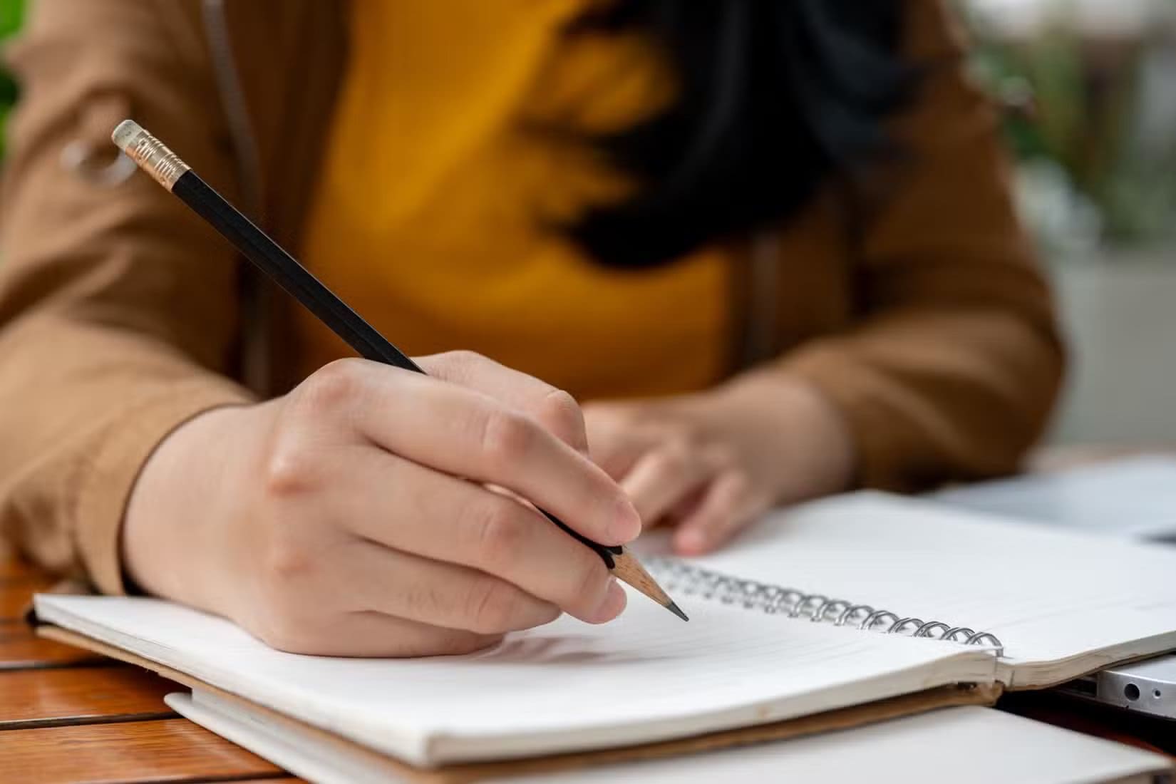 a-close-up-image-of-a-woman-holding-a-pencil-writing-something-in-her-notebook دليل الطالب لاستخدام ChatGPT بذكاء أثناء الدراسة الجامعية