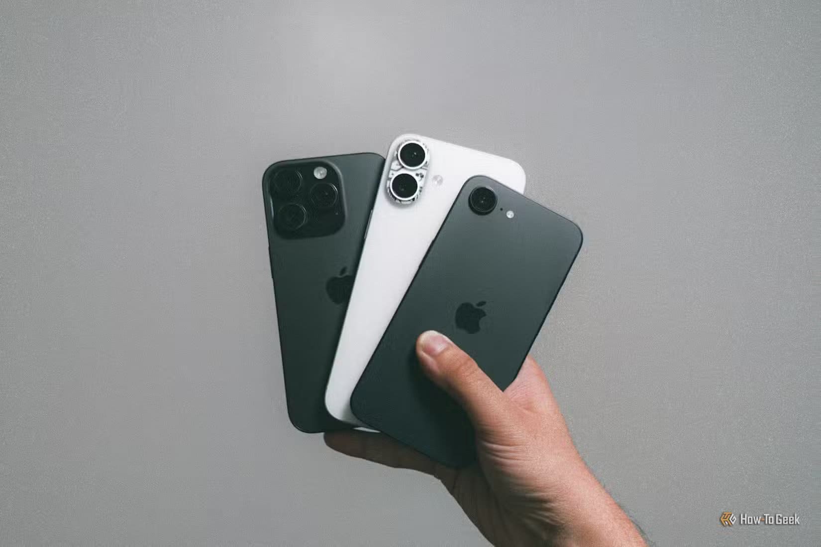 iphone-16e-with-iphone-16-plus-and-iphone-16-pro-in-hand-against-grey-wall-1 أسباب تجعل تجربة استخدام iPhone أقل جاذبية مما كانت عليه