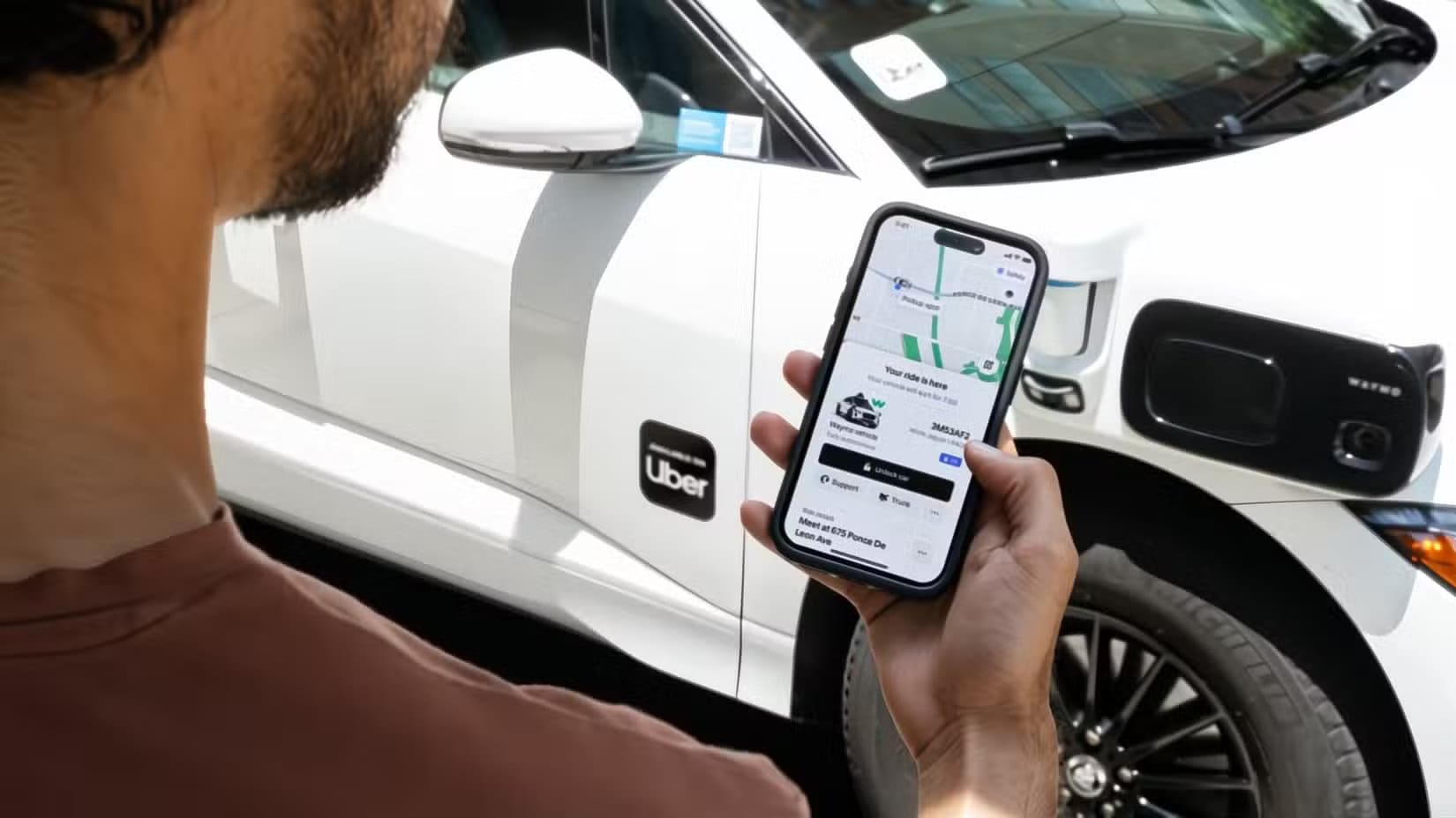 a-man-looking-at-his-uber-app-next-to-a-car-with-the-uber-logo-on-it أسباب تجعل iPod Touch مع الهاتف العادي مزيج محمول مثالي